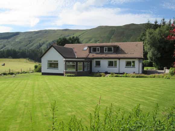 White forest lodge with large lawn set against rolling green hills under a blue sky.