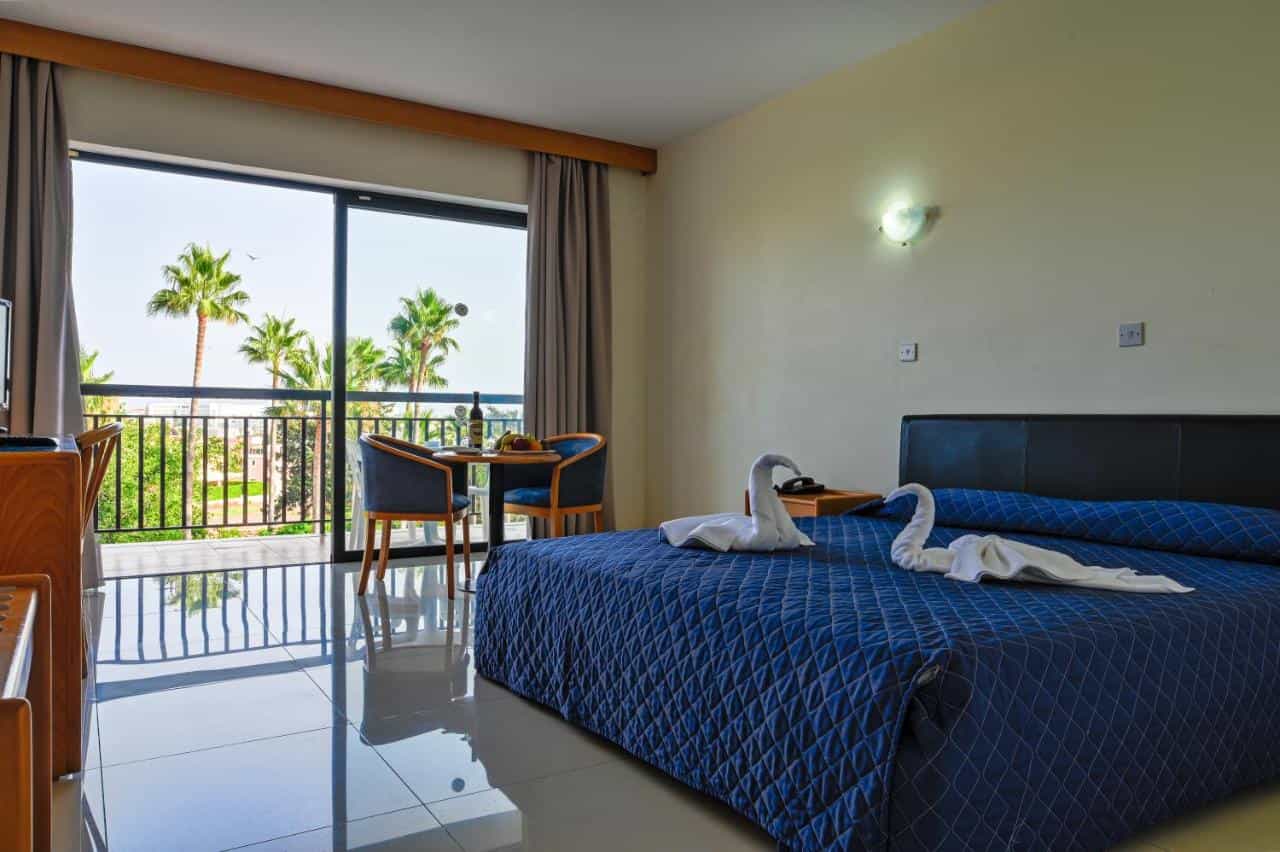 Hotel room with blue bedding, towel swans, and balcony view of palm trees
