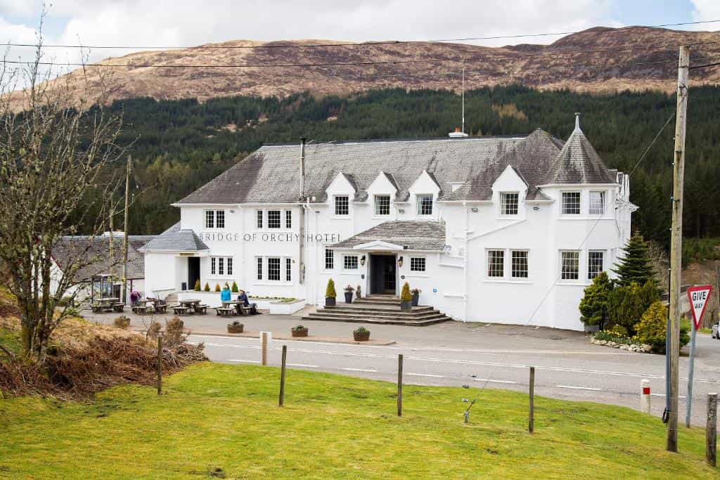Bridge of Orchy Hotel, a white building, set against forested mountainsides.