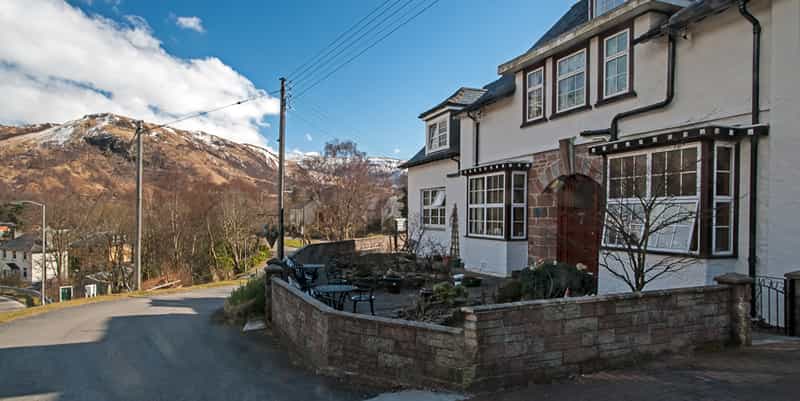 White Bed & Breakfast building with outdoor seating near brown, snow-dusted mountain.
