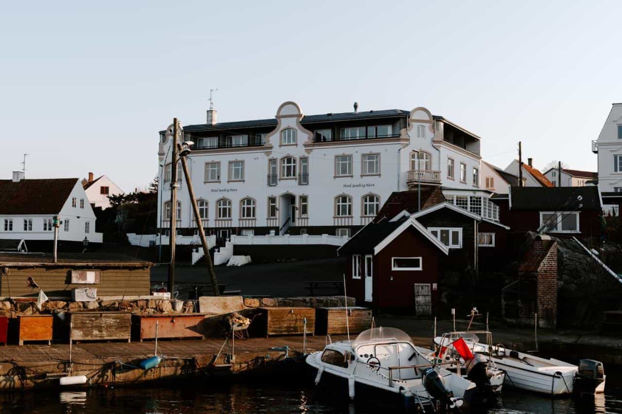 Boats docked in harbor before Hotel Sandvig Havn buildings in coastal town.