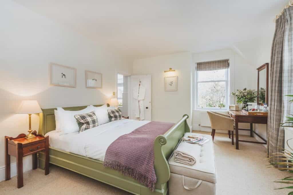 Bedroom in The Craigellachie Hotel with green sleigh bed, plaid pillows, and writing desk.
