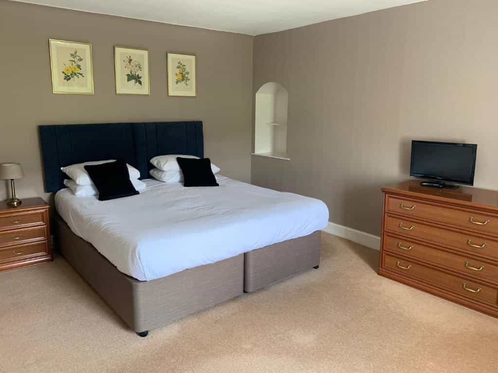 Bedroom with double bed, wooden dresser, small TV, and floral artwork on tan walls.