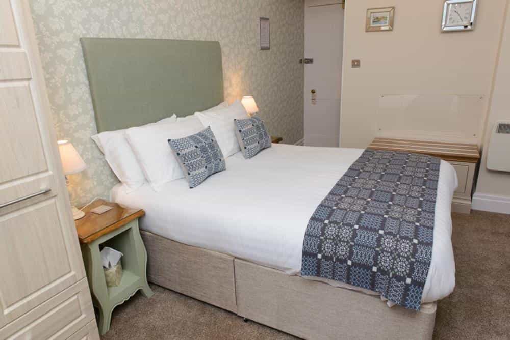 Hotel bedroom with double bed, patterned pillows, white linens, and light green headboard