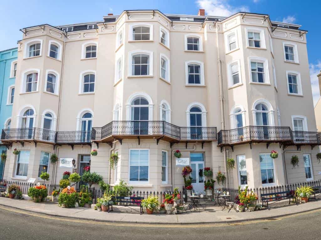 Giltar Hotel facade with bay windows, balconies, and colorful flower displays on a sunny day.