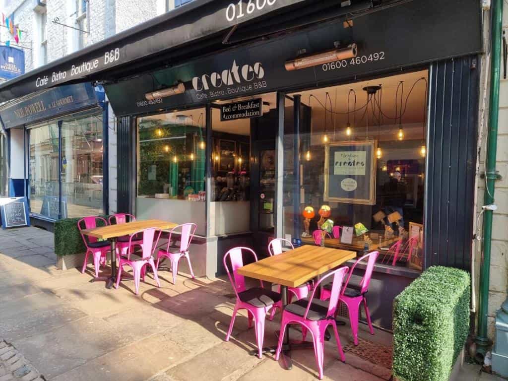 Cafe Bistro Boutique B&B exterior with outdoor seating featuring pink metal chairs and wooden tables.