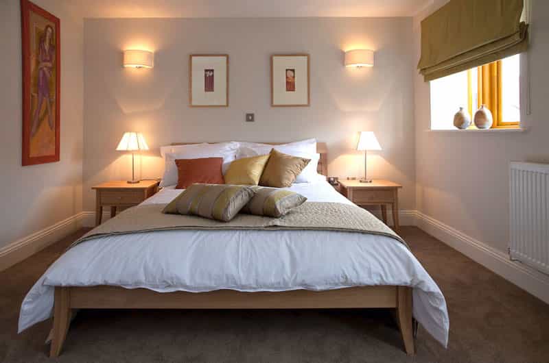 Cozy bedroom with wooden bed frame, white linens, and warm lighting from bedside lamps.
