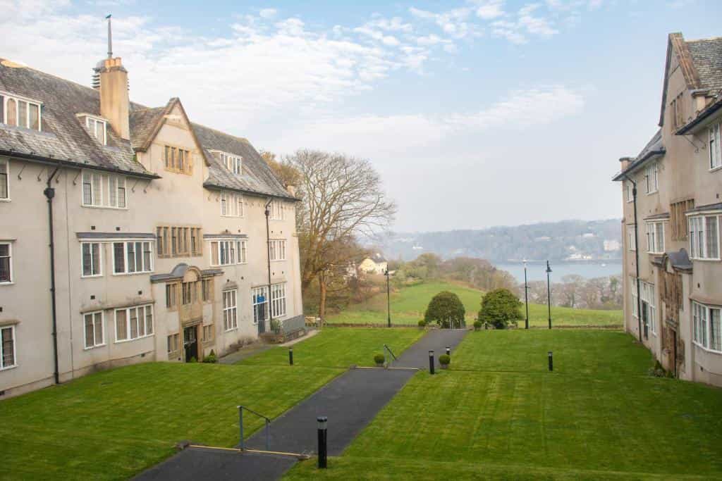 Large stone buildings flanking a manicured lawn overlooking a wide river estuary.