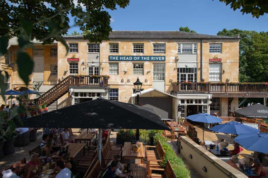 Outdoor dining patio at The Head of the River pub with patrons seated under umbrellas.