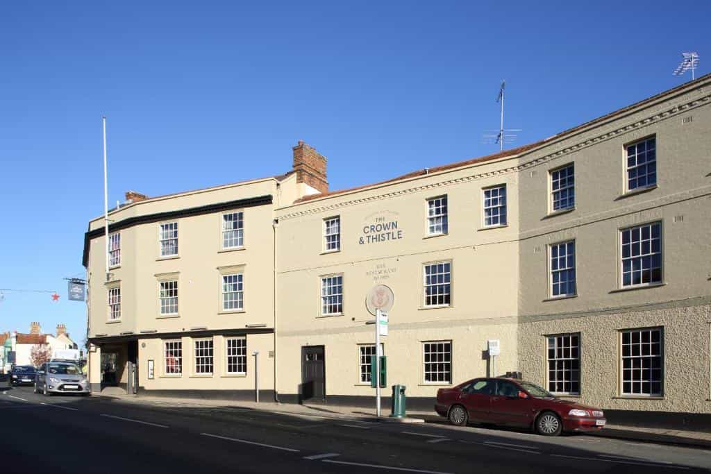 The Crown & Thistle pub building on a street with parked cars under a clear blue sky.
