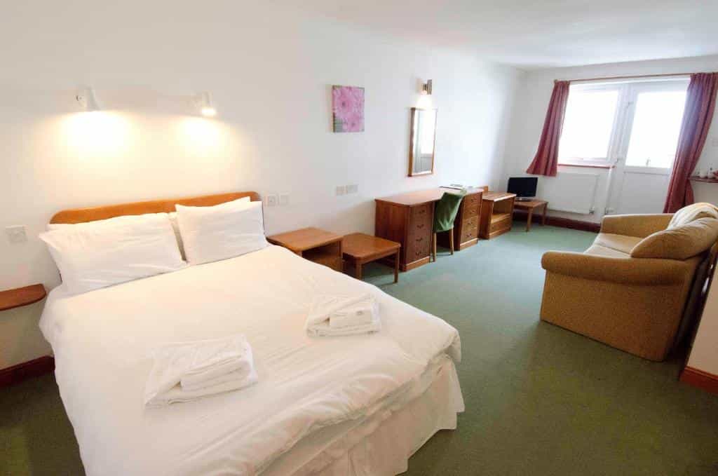 Bedroom in Seacote Hotel with double bed, wooden desk, and sofa on green carpet.