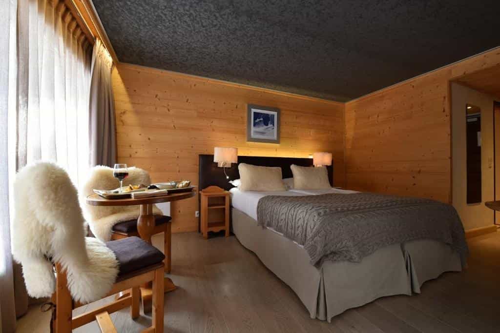 Cozy hotel room with wood paneling, twin beds, and a small table with wine and snacks.