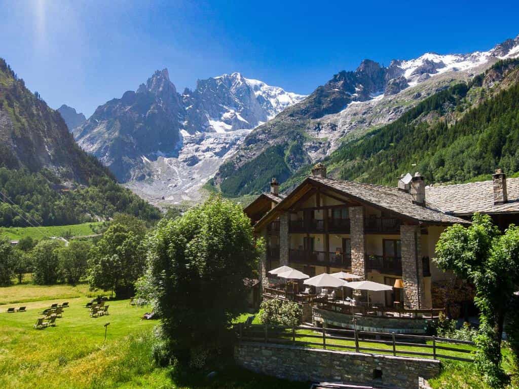 Chalet style hotel with outdoor terrace in green valley beneath snow-capped mountains