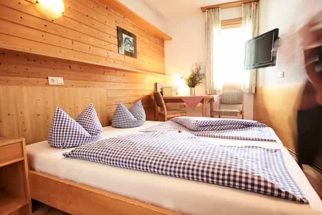 Hotel room with wooden walls, blue checkered bedding, and a small desk at Berghotel Rudolfshütte.