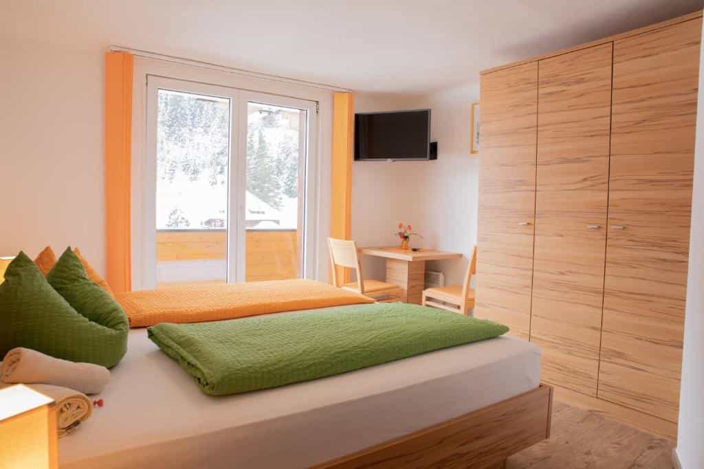 Hotel room with green and orange bedding, wooden furniture, and snowy view outside.