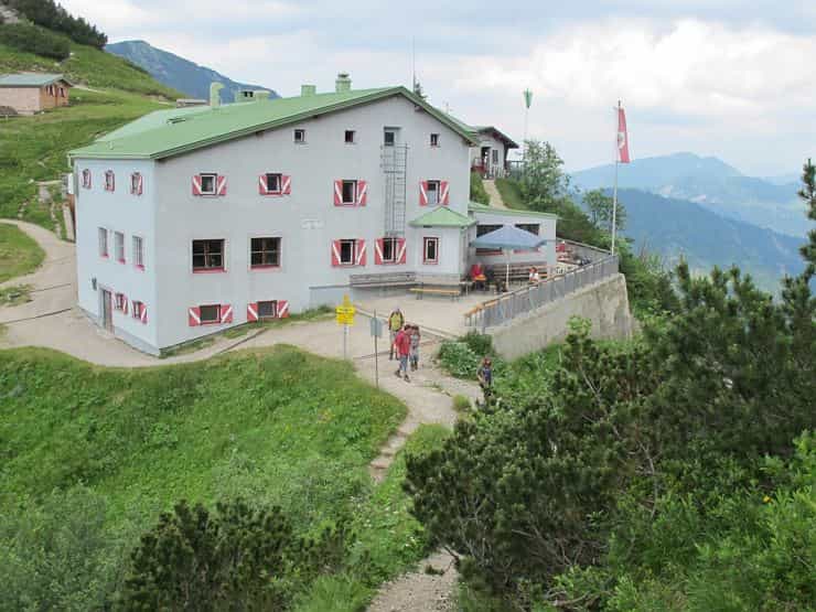 Stripsenjochhaus mountain hut with hikers on a dirt path overlooking alpine scenery.