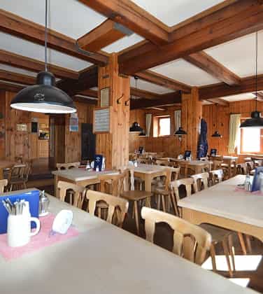 Rustic dining room with wood paneling, exposed beams, and wooden tables and chairs at Knorrhütte.