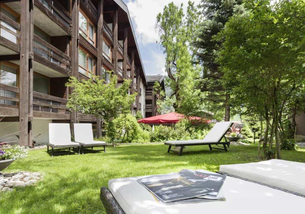 Lawn area with white lounge chairs beside a wooden alpine-style hotel building.