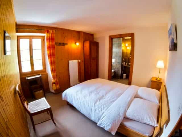 Bedroom with wood paneling, white bedding, and doorway to bathroom at Hôtel de La Sage.