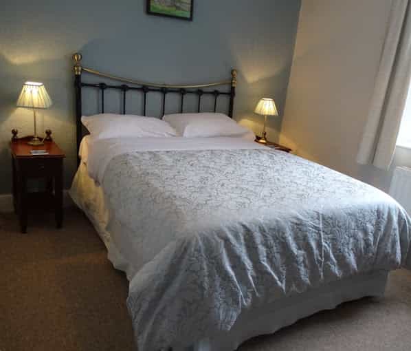 Double bed with white linens and patterned coverlet, flanked by nightstands with lamps in a room.