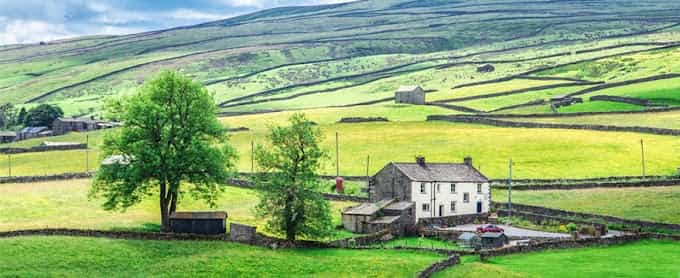 Farmhouse nestled in green rolling hills divided by numerous dry stone walls