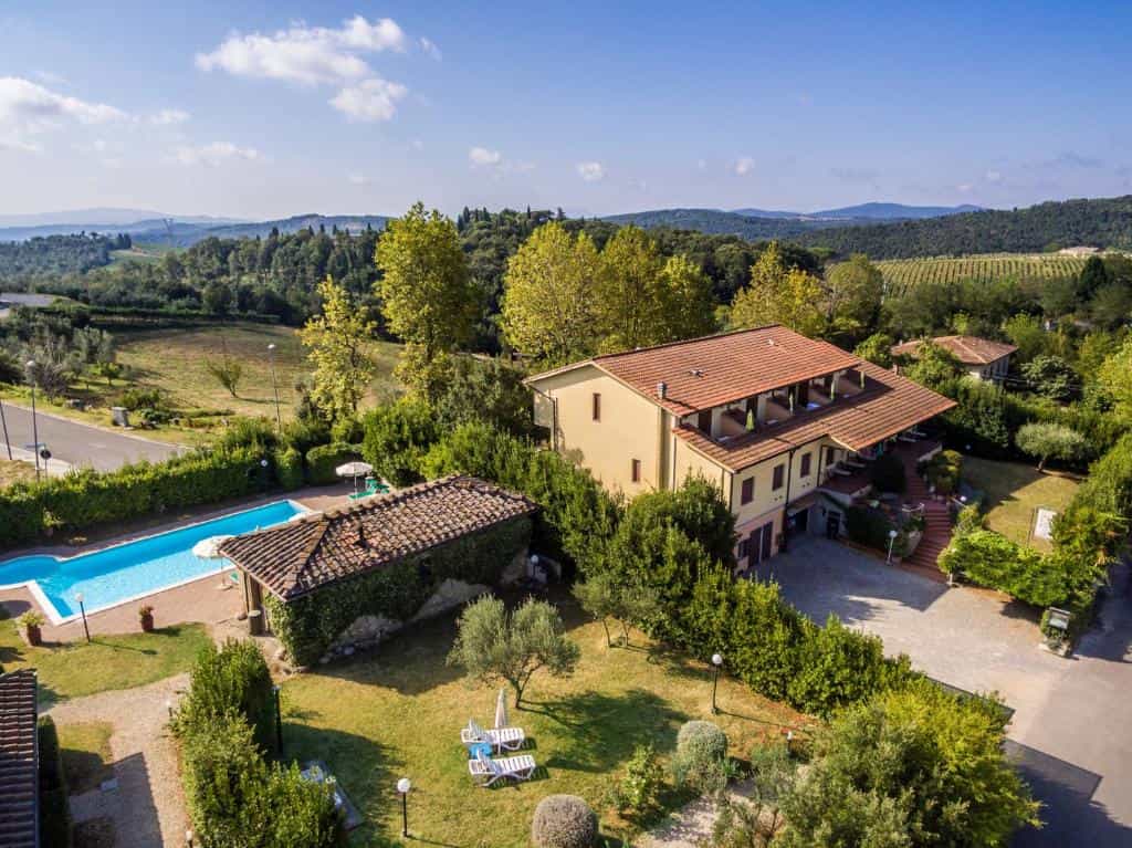Yellow villa with swimming pool surrounded by lush greenery and rolling hills under blue sky.