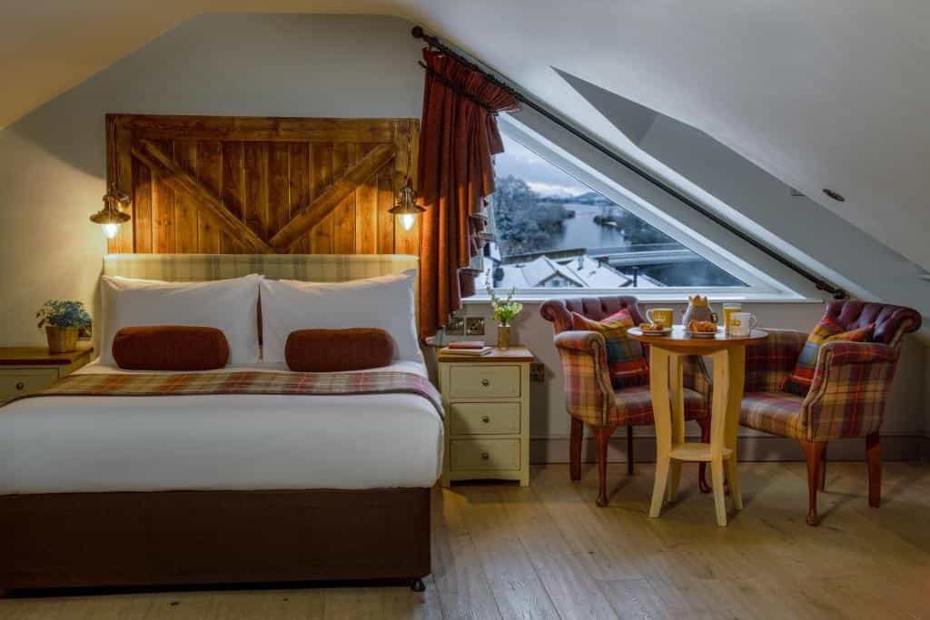 Bedroom with wooden headboard, plaid chairs, and view of snowy river from attic window at The Crown Inn Pooley Bridge.