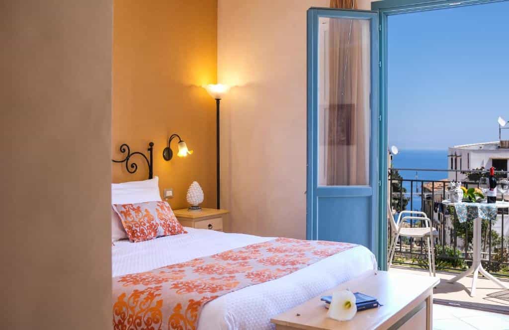 Bedroom with orange accents opening to a balcony overlooking the blue sea.
