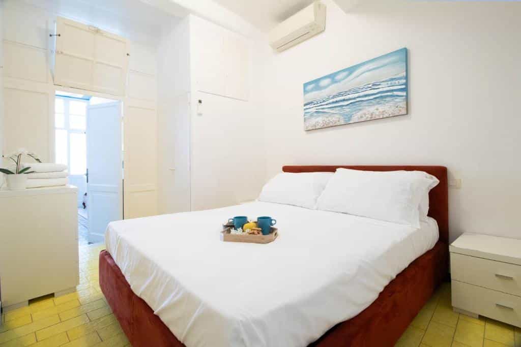 Bedroom with white linens, tray of breakfast, and beach art, yellow tiled floor.