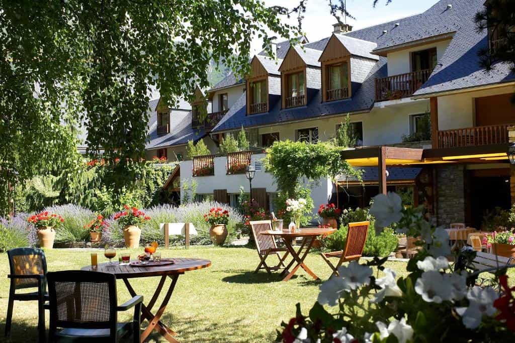 Hotel Mir-ena garden with outdoor tables, lawn, and alpine-style building in summer.