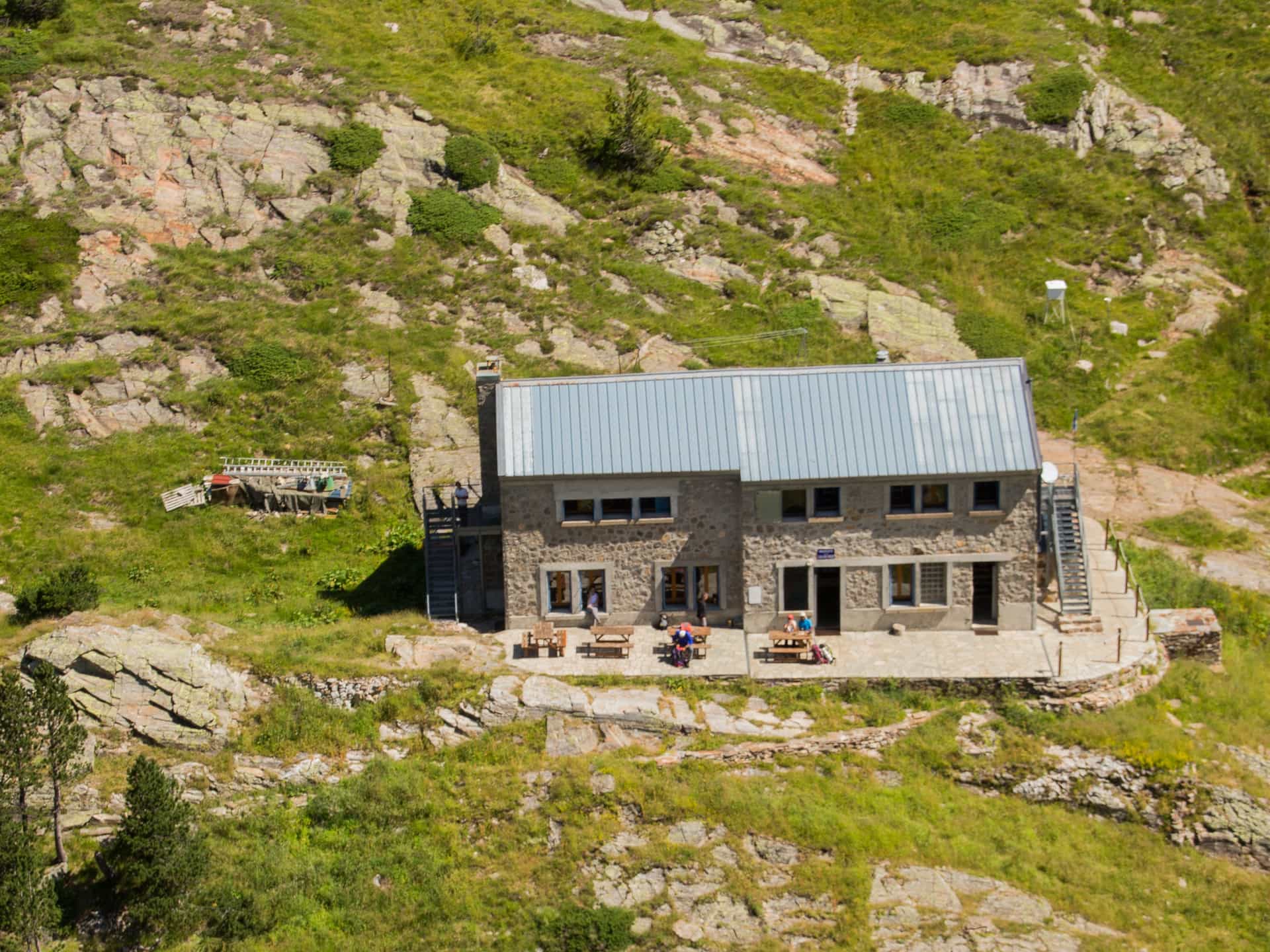 Stone mountain refuge Le Refuge d'Espingo with metal roof on grassy slope in summer