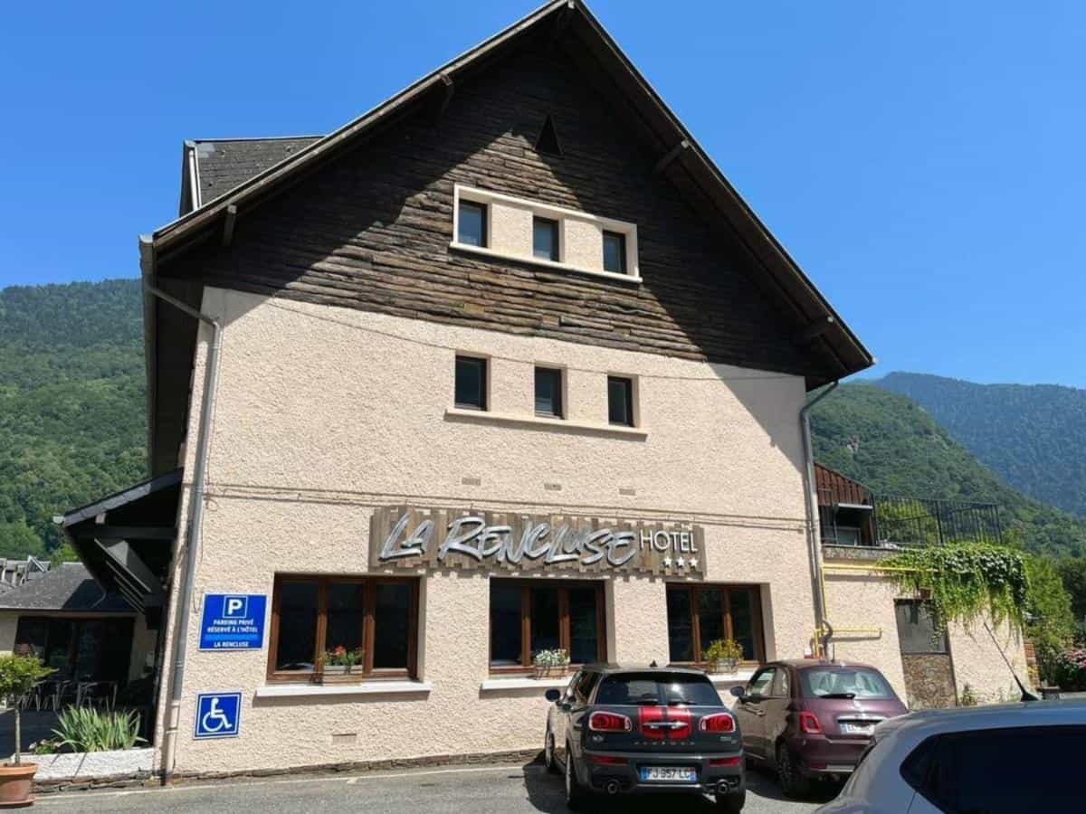 Hôtel La Rencluse with cars parked outside, set against lush green mountains.