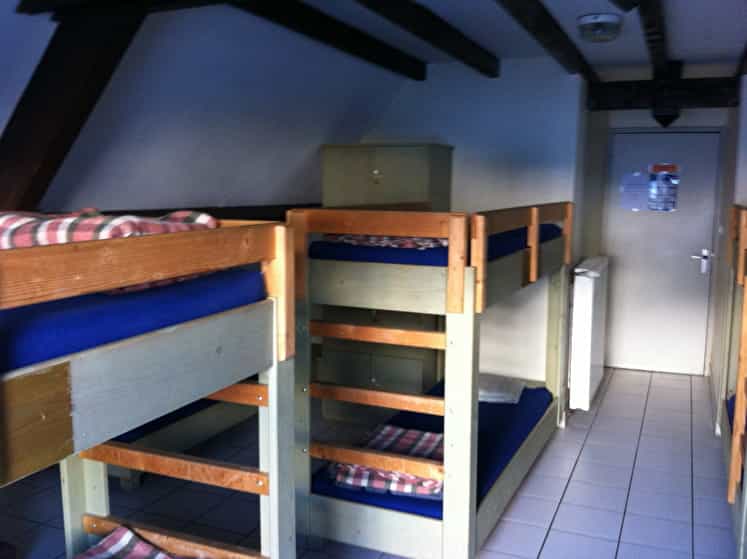 Bunk beds with blue mattresses and plaid blankets in an attic dormitory room at Refugio de la Grange de Holle.