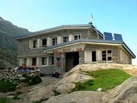 Refuge d'Oulettes d'Oulettes stone mountain hut with solar panels and hikers resting outside.