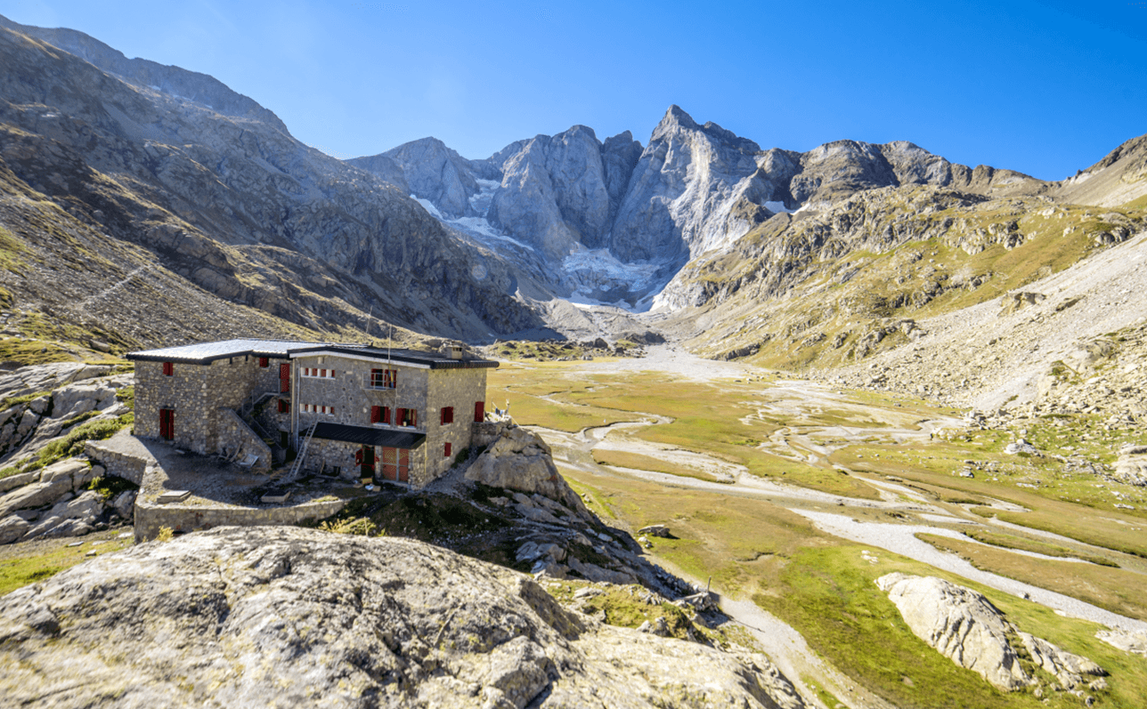 Refugio de Oulèttes stone mountain refuge beneath rugged peaks with a glacier and valley floor.