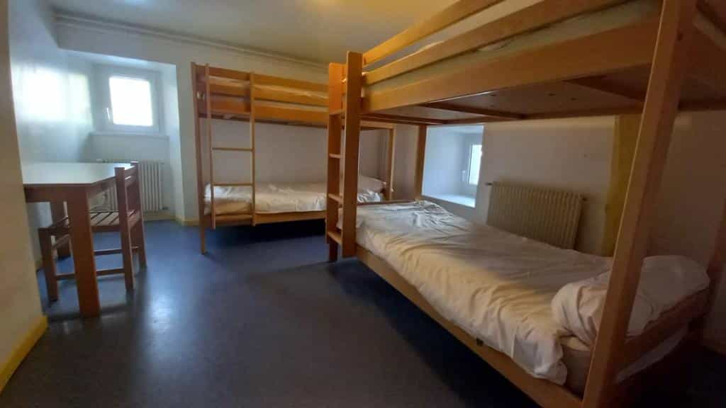 Bunk beds and wooden table in simple dormitory room at Laberouat Refuge