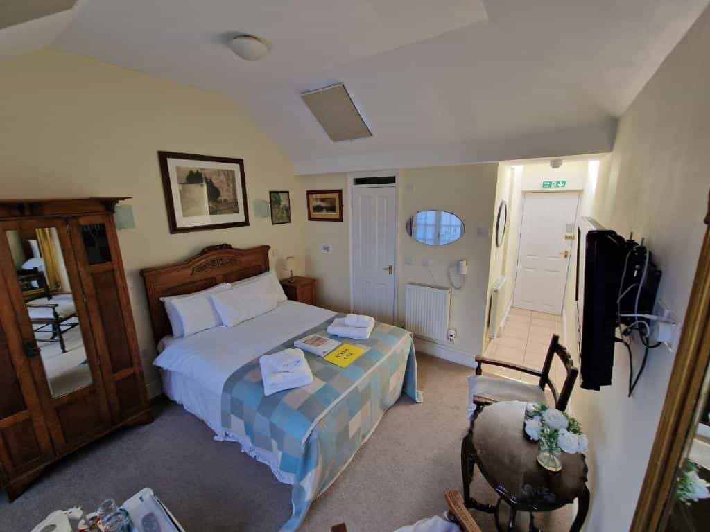 Bedroom in The Black Horse Inn with wooden furniture, white bedding, and blue plaid throw.