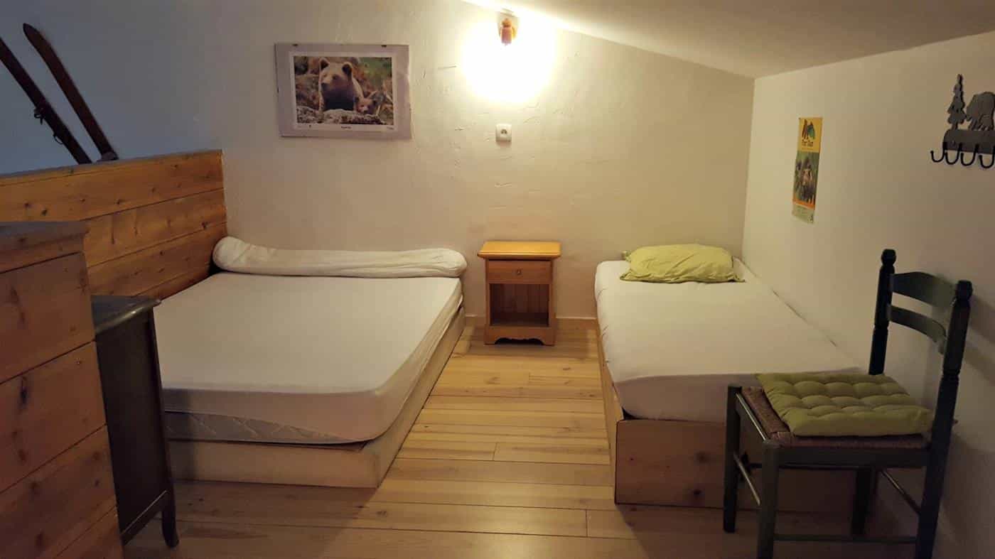 Bedroom with two beds, wooden floors, bear picture, and skis hanging on the wall.