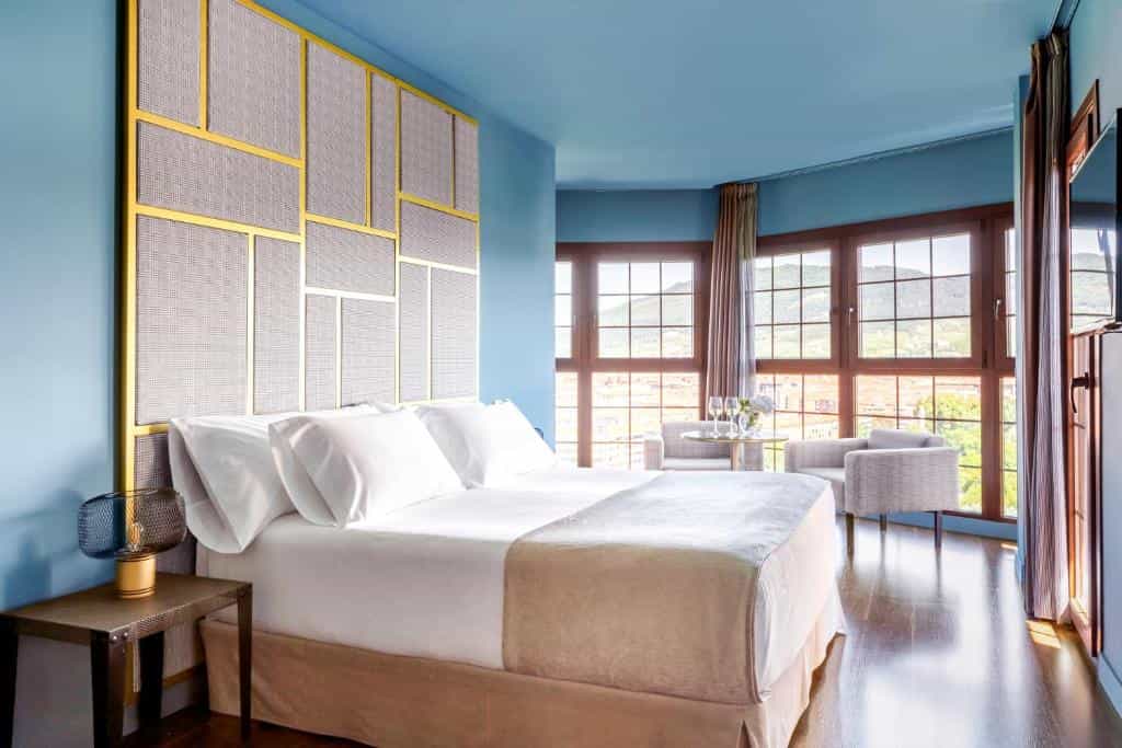 Hotel bedroom with blue walls, large windows showing mountains, and modern decor