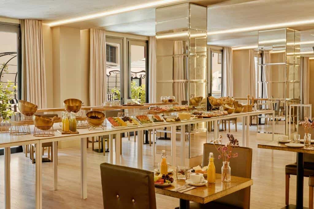 Buffet breakfast spread with fruit, cheese, and bread in a modern dining room with mirrored pillars.