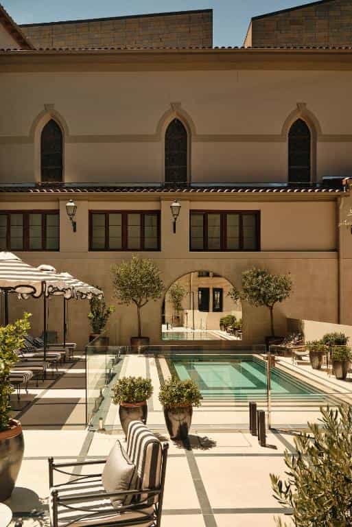 Courtyard pool area with striped umbrellas, potted trees, and arched architectural details.