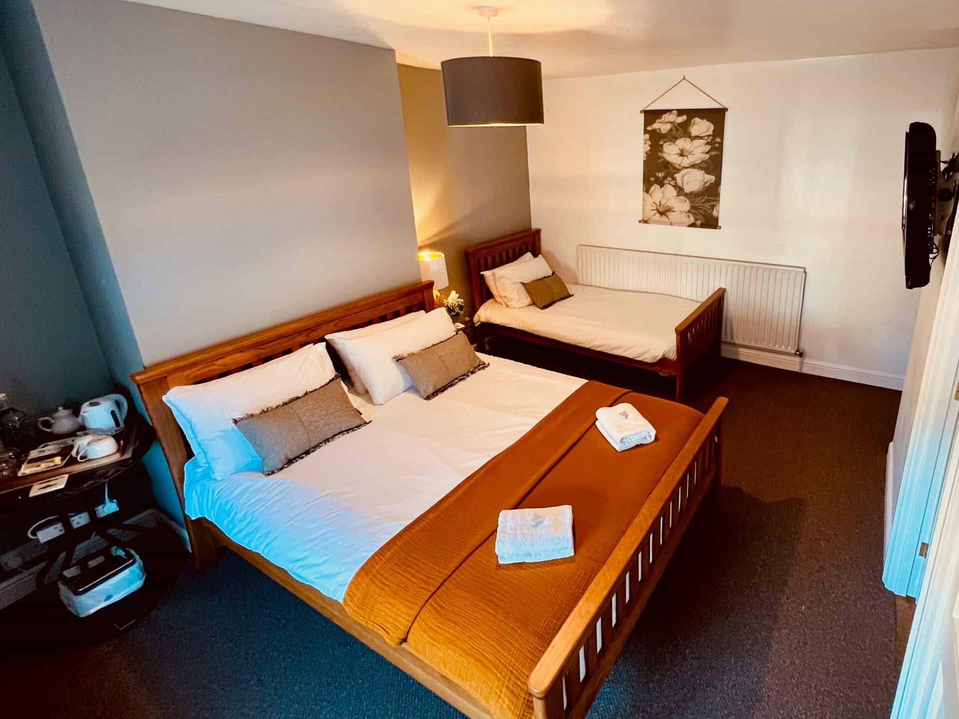 Bedroom with wooden double bed, single bed, white linens, and floral wall hanging.