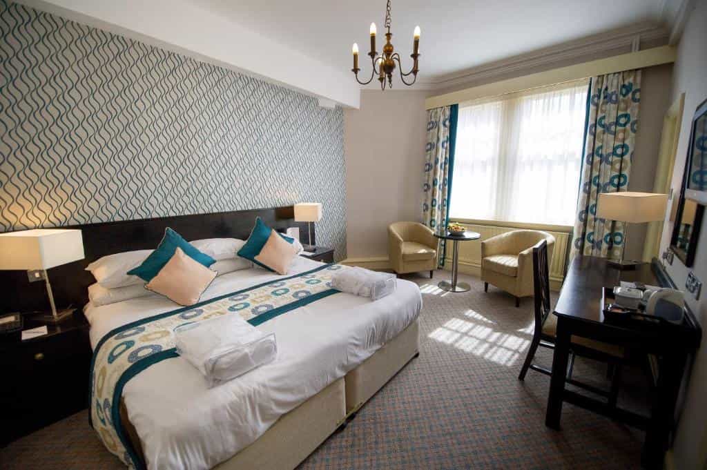 Bedroom in Crown & Mitre Hotel with patterned wallpaper, white bedding, and seating area.