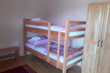 Wooden bunk beds with pink striped bedding inside a simple room with a wooden wardrobe.