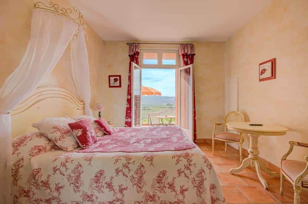 Bedroom with canopy bed and balcony view of rolling hills and orange umbrella.
