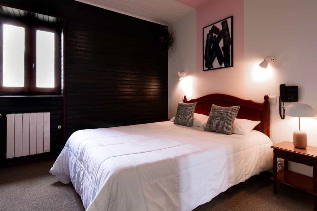 Bedroom with white bedding, dark wood accent wall, window, and bedside lamp in Loubressac.
