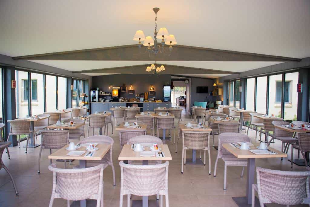 Dining room with wicker chairs and set tables, bright interior with large windows.