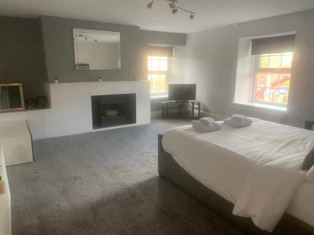 Bedroom with white bedding, fireplace, and view of red bridge structure through window.