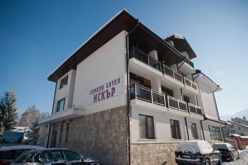 Family Hotel Iskar building exterior with snow on parked cars under a clear blue sky.