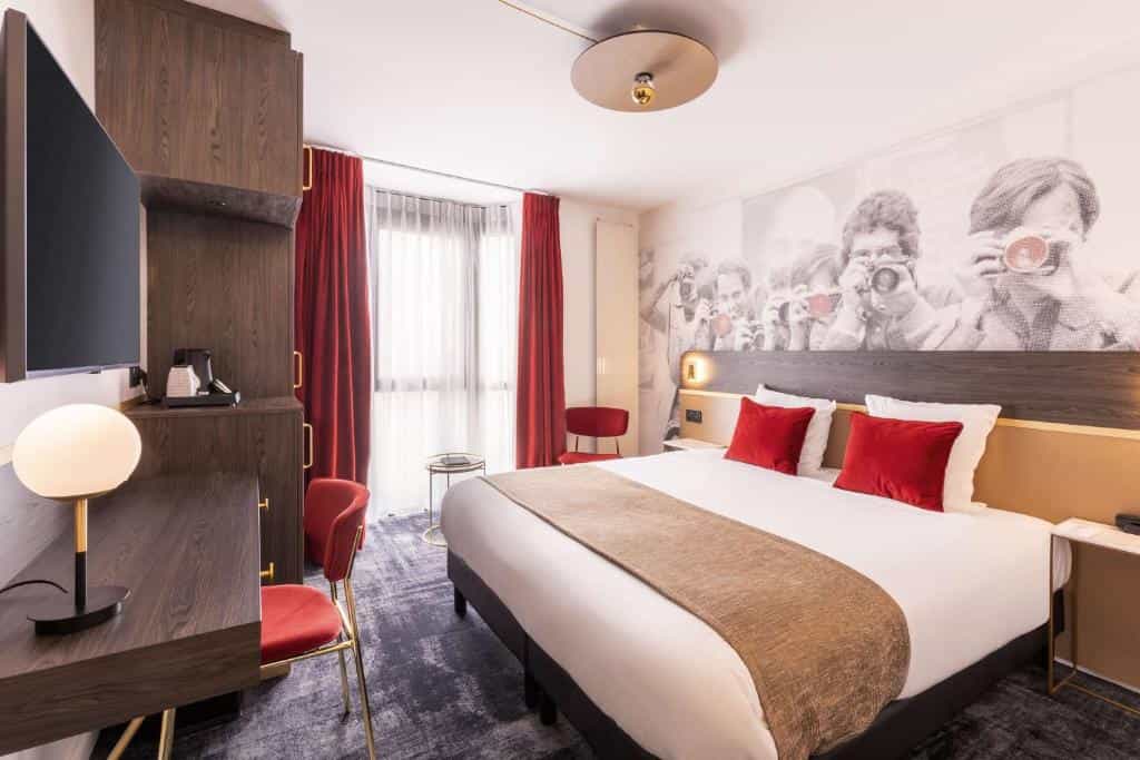 Hotel room with white bedding, red pillows, dark wood furniture, and a wall mural of photographers.